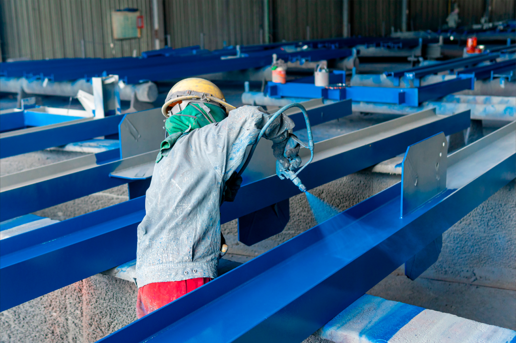 Pintor industrial com EPI aplicando tinta azul de alta qualidade para estruturas metálicas da Vinilak em viga de aço com pistola. Garantia anticorrosiva.